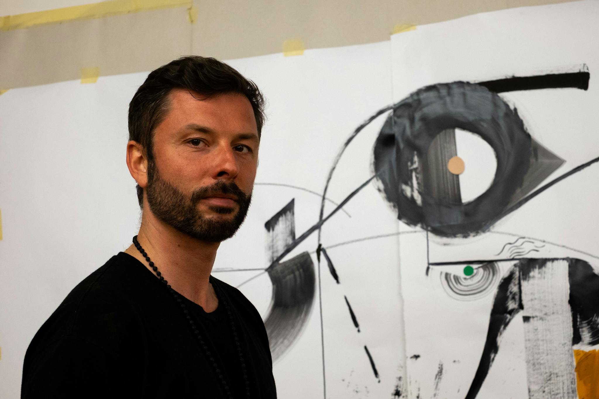 Tomek Sadurski is photographed in front of an abstract image featuring black designs.