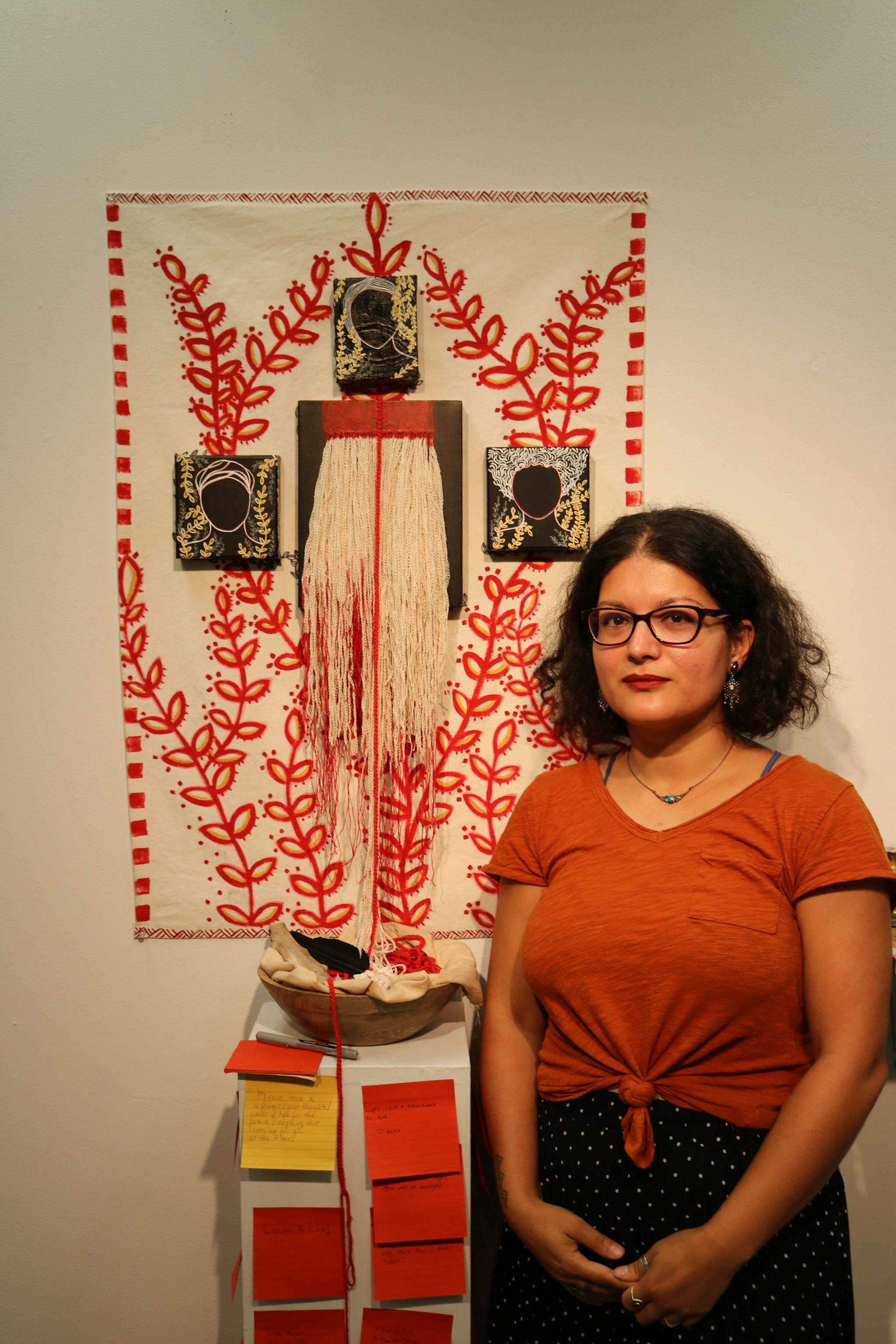 Ankana stands in front of a shrine she made, which features post-it notes and a fabric work hanging from the wall.
