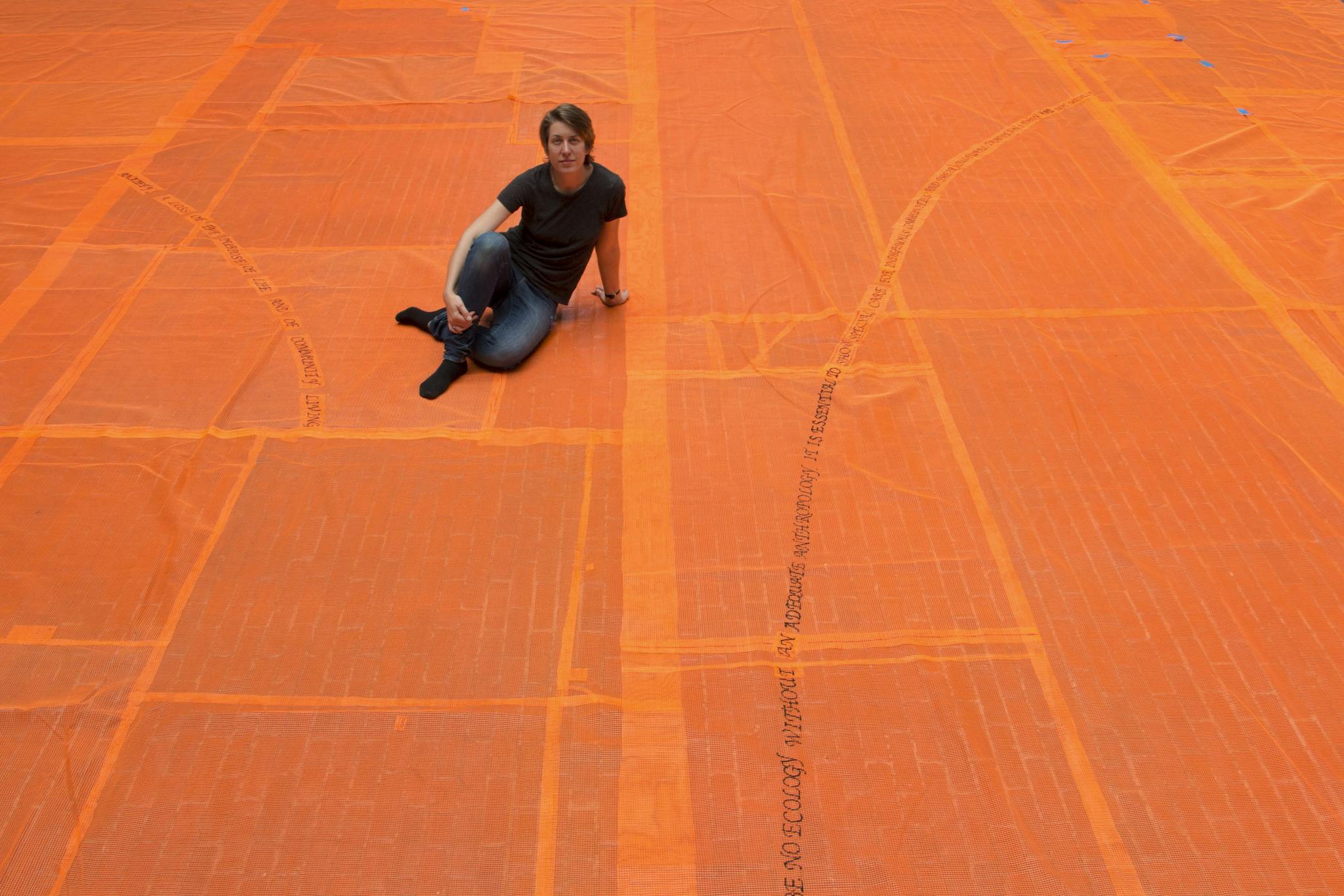 Stephanie Cardon sits on the orange, embroidered netting featured in her installation.