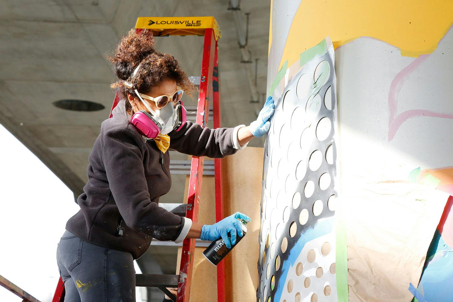 Silvia Lopez Chavez works on a mural project, while a red ladder appears behind her.