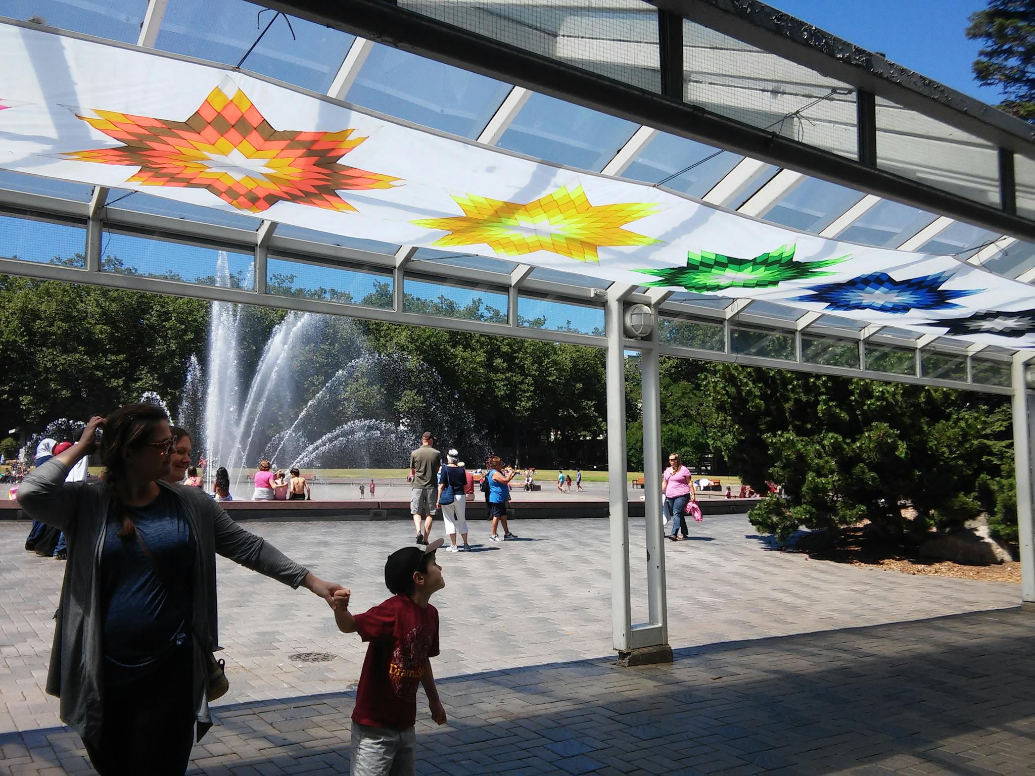 Visitors gather near a colorful, overhanging banner, while a fountain stands in the background.