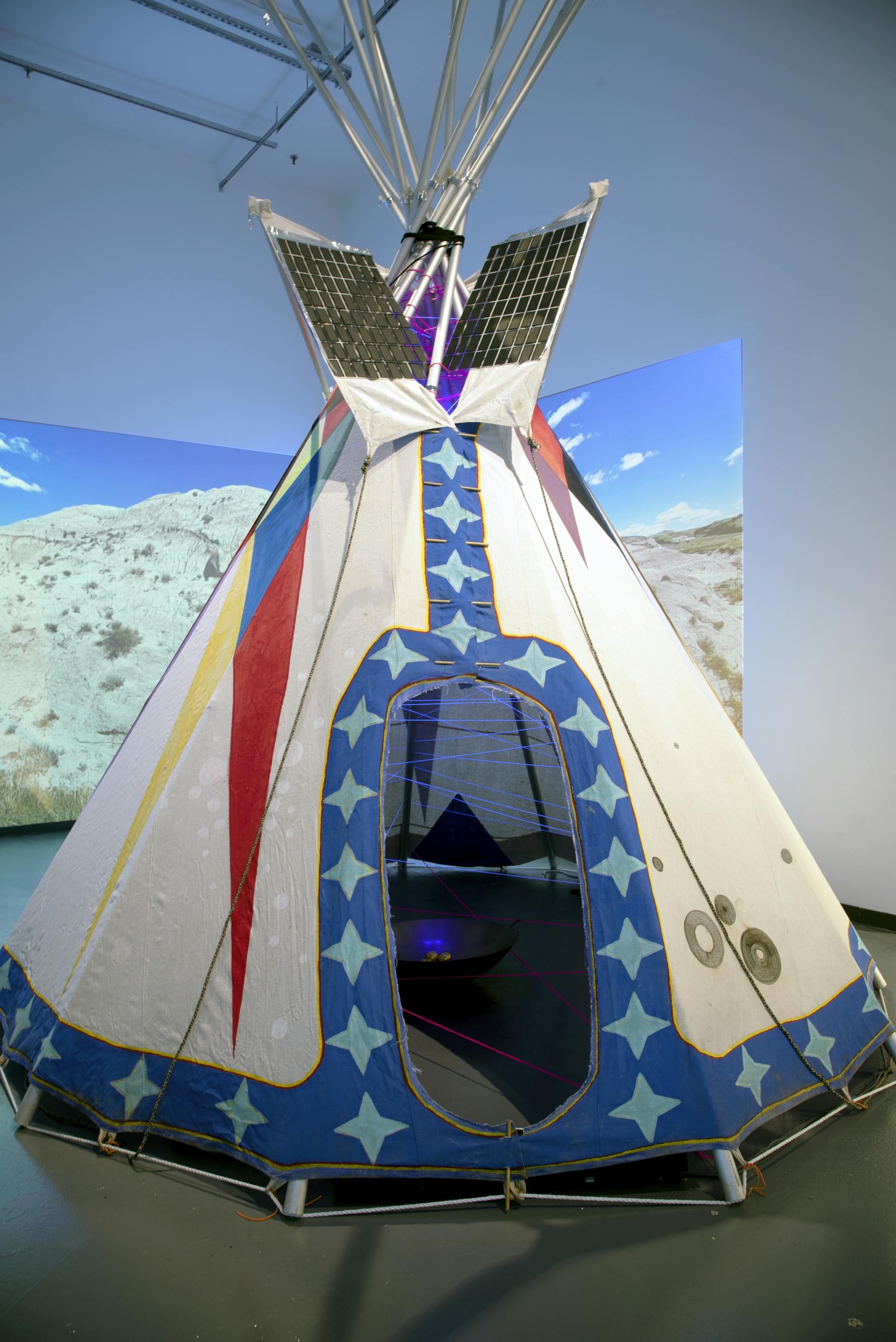 A large, colorful cloth tipi with collapsible metal support poles stands tall.