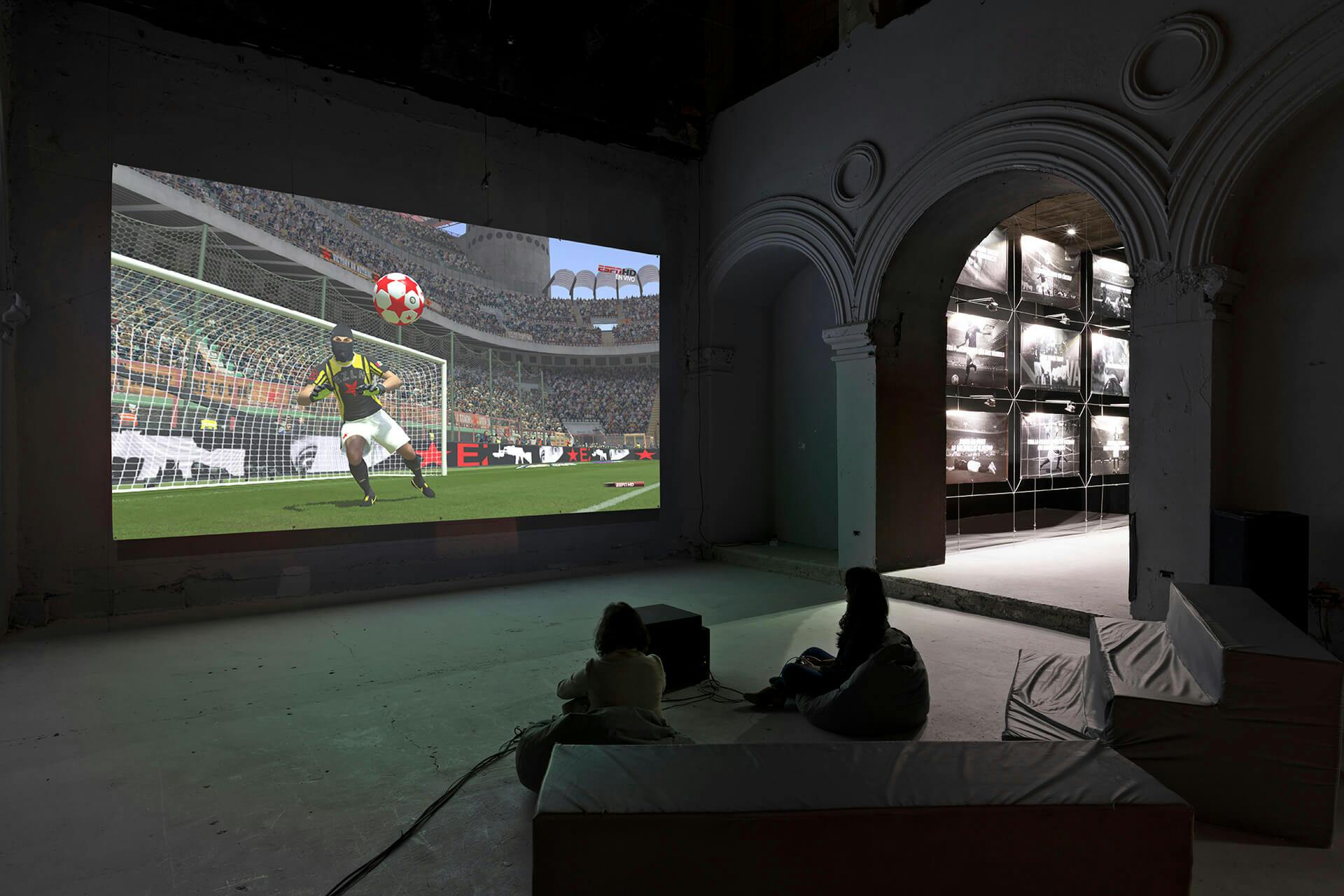 Viewers watch a screen displaying a soccer game, as part of an installation.