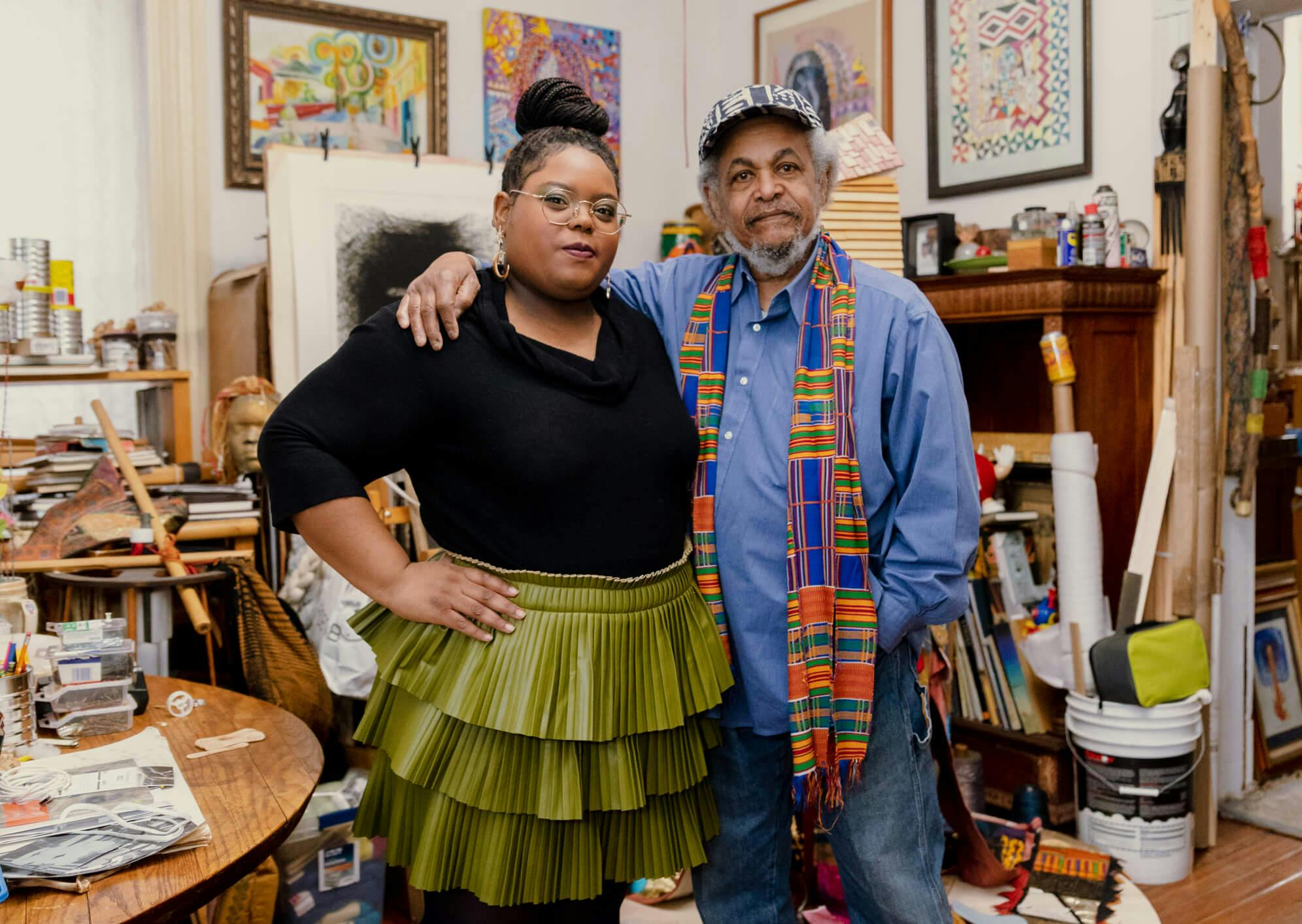 Chanel Thervil and Napoleon Jones-Henderson stand in an artist studio with an array of materials in the background.
