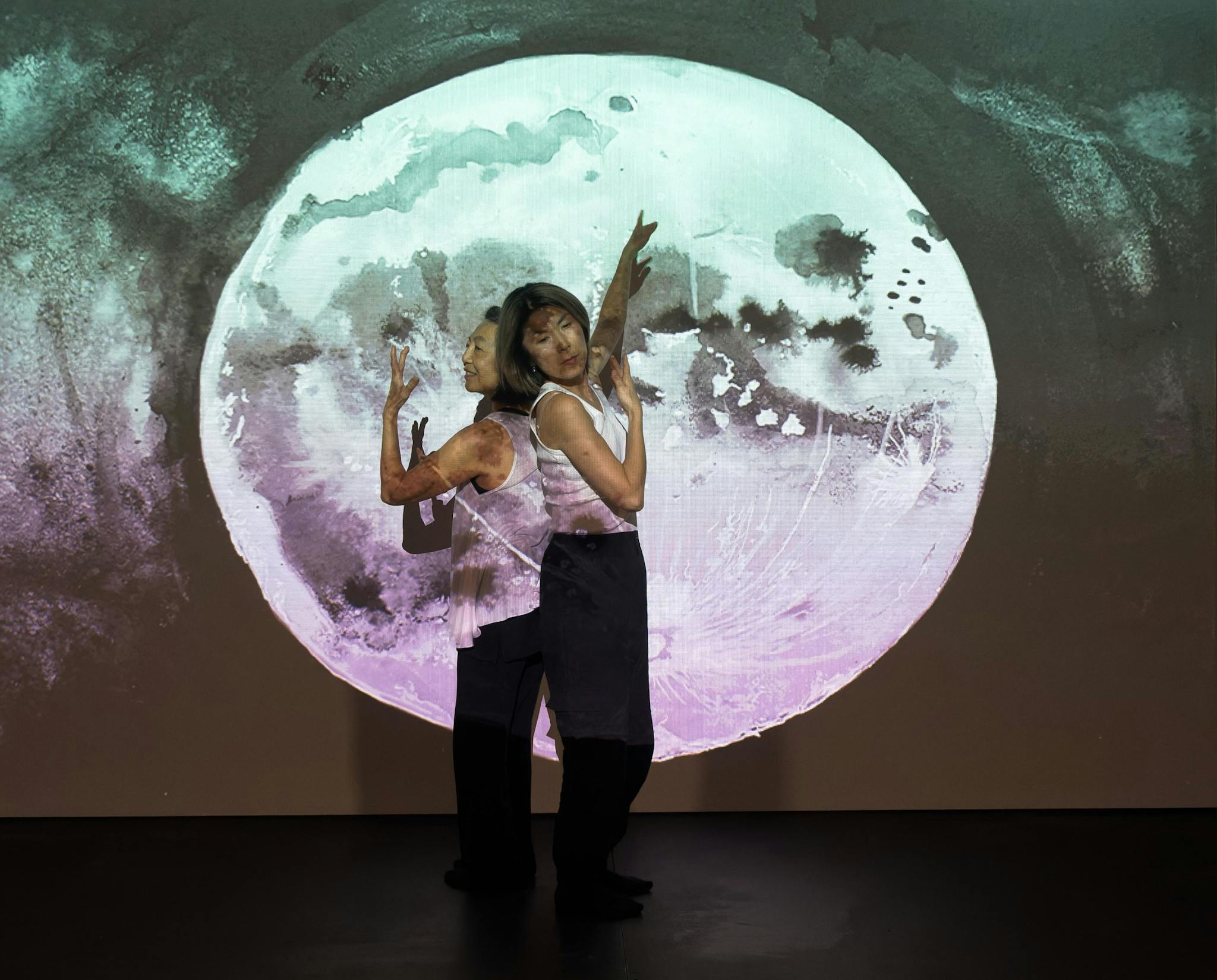 Fernadina Chan and Soyoung L. Kim perform in front of a full moon set against a dark sky.