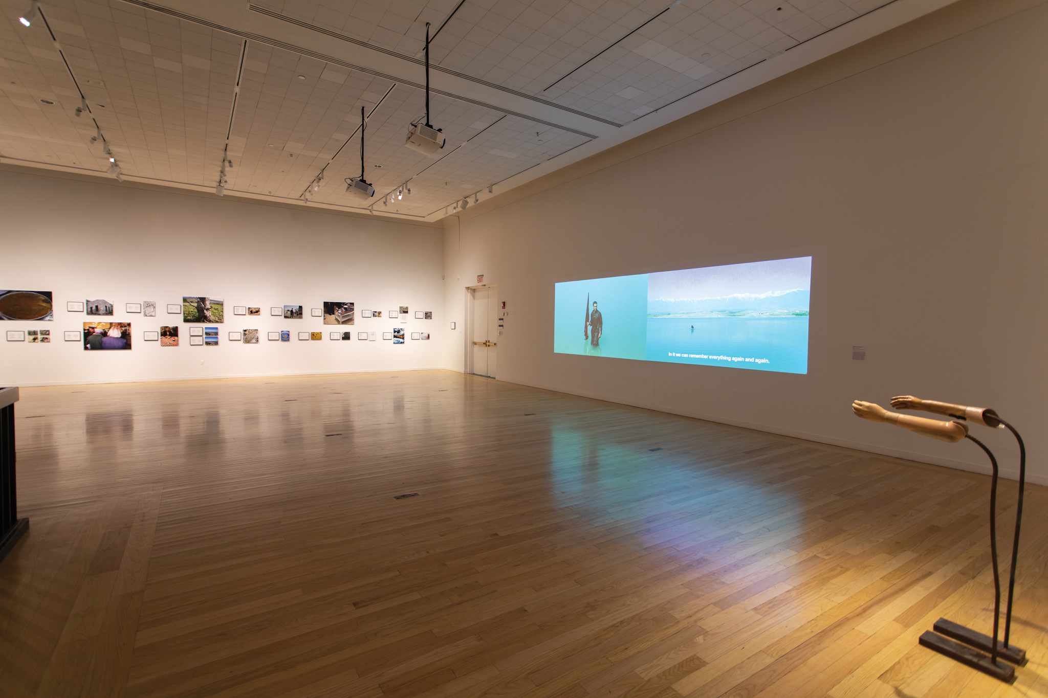 A bright blue video projection on the far right wall is part of an exhibit at Tufts University Art Galleries.
