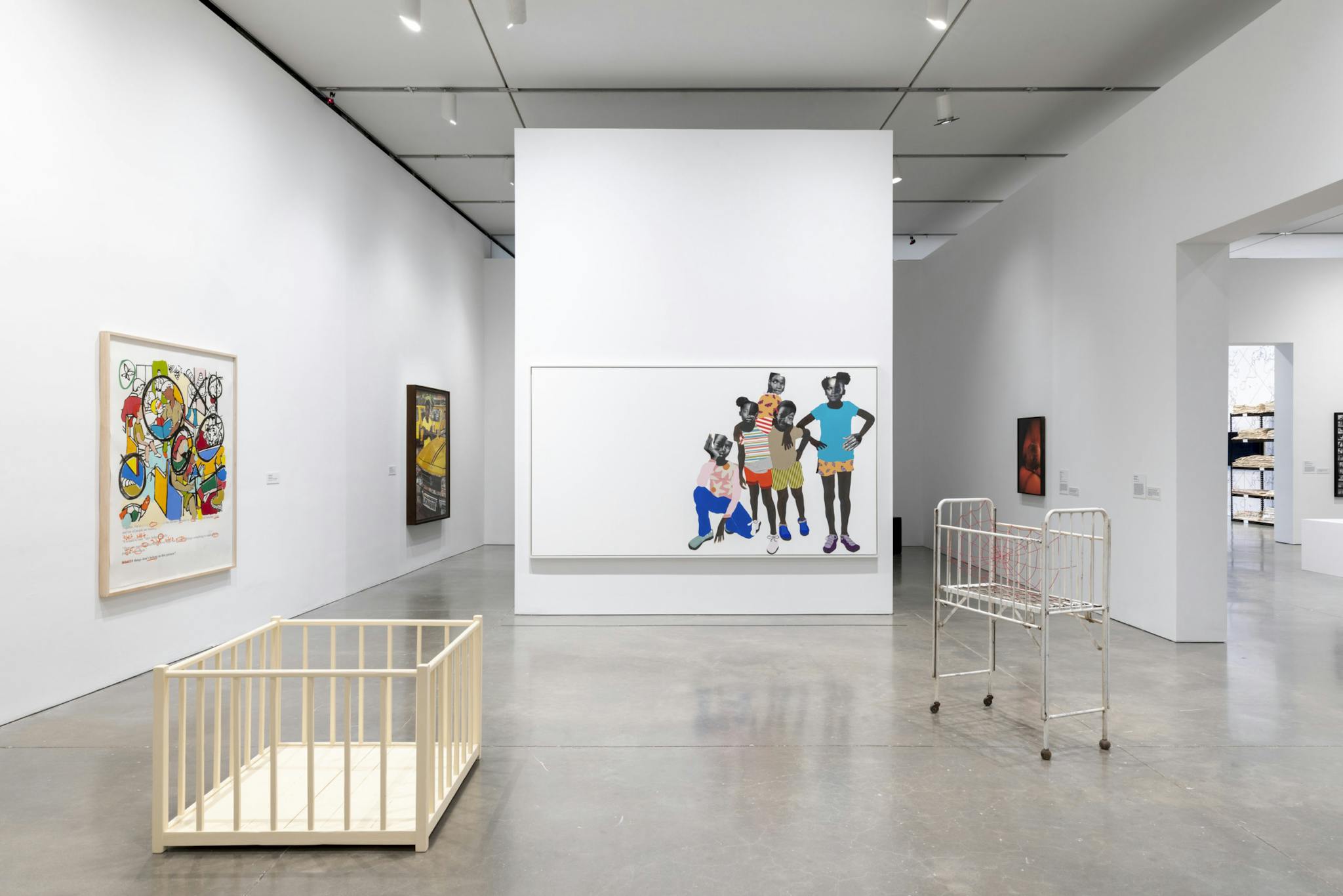 An installation features a beige crib and a colorful design of children, set against a white wall.