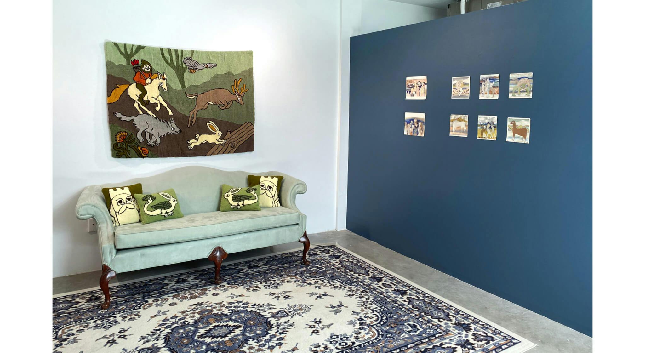 A green couch with pillows stands beneath an artwork that features fairytale-like characters.