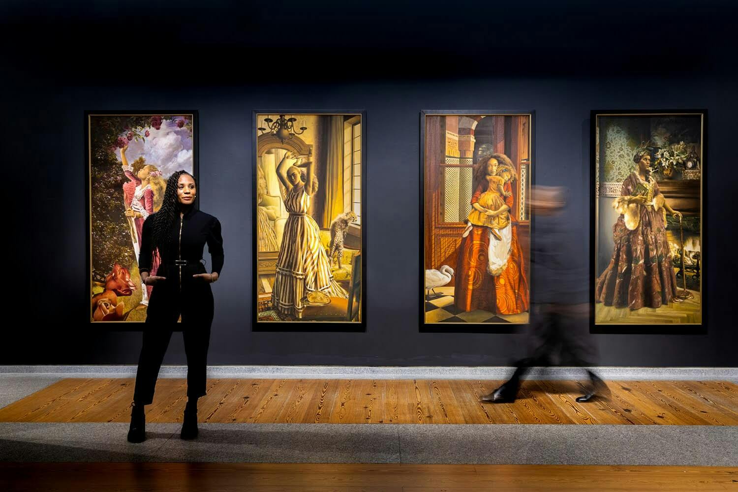 Elizabeth Colomba stands in front of a series of fairytale inspired images, set against a navy blue wall.