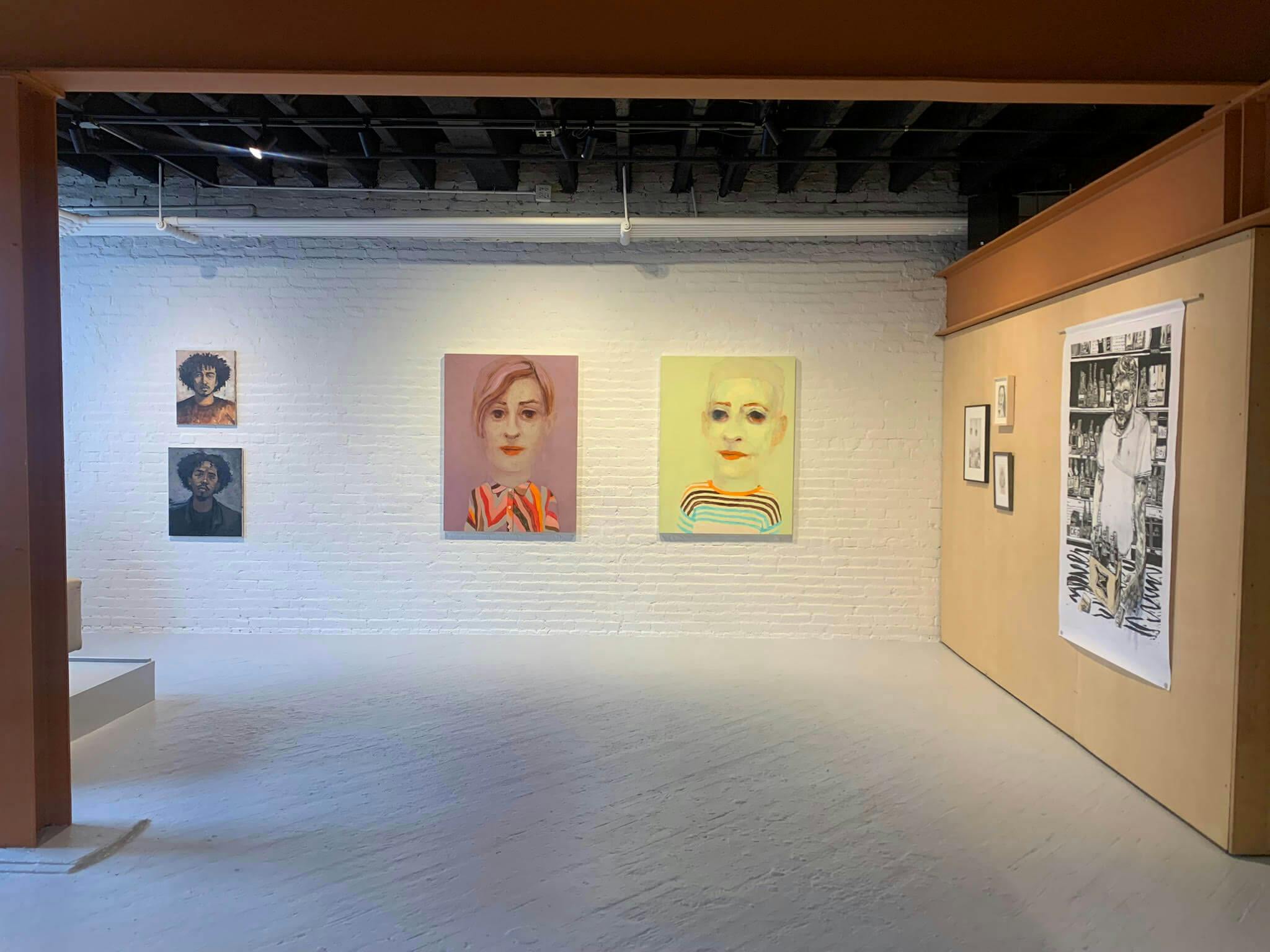 The images of faces are displayed on canvases, set against a white brick wall at Gallery VERY.