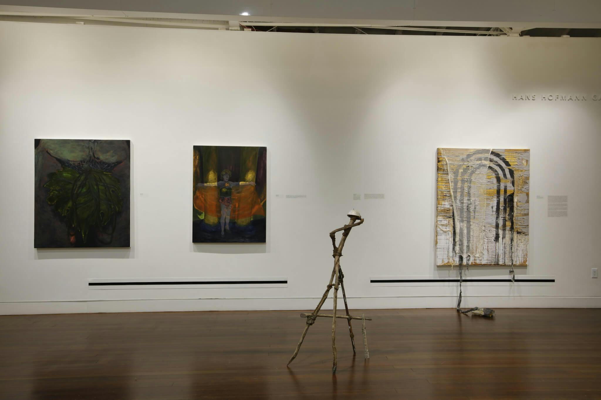 Three paintings adorn the walls of a gallery, while a sculpture stands in the middle.