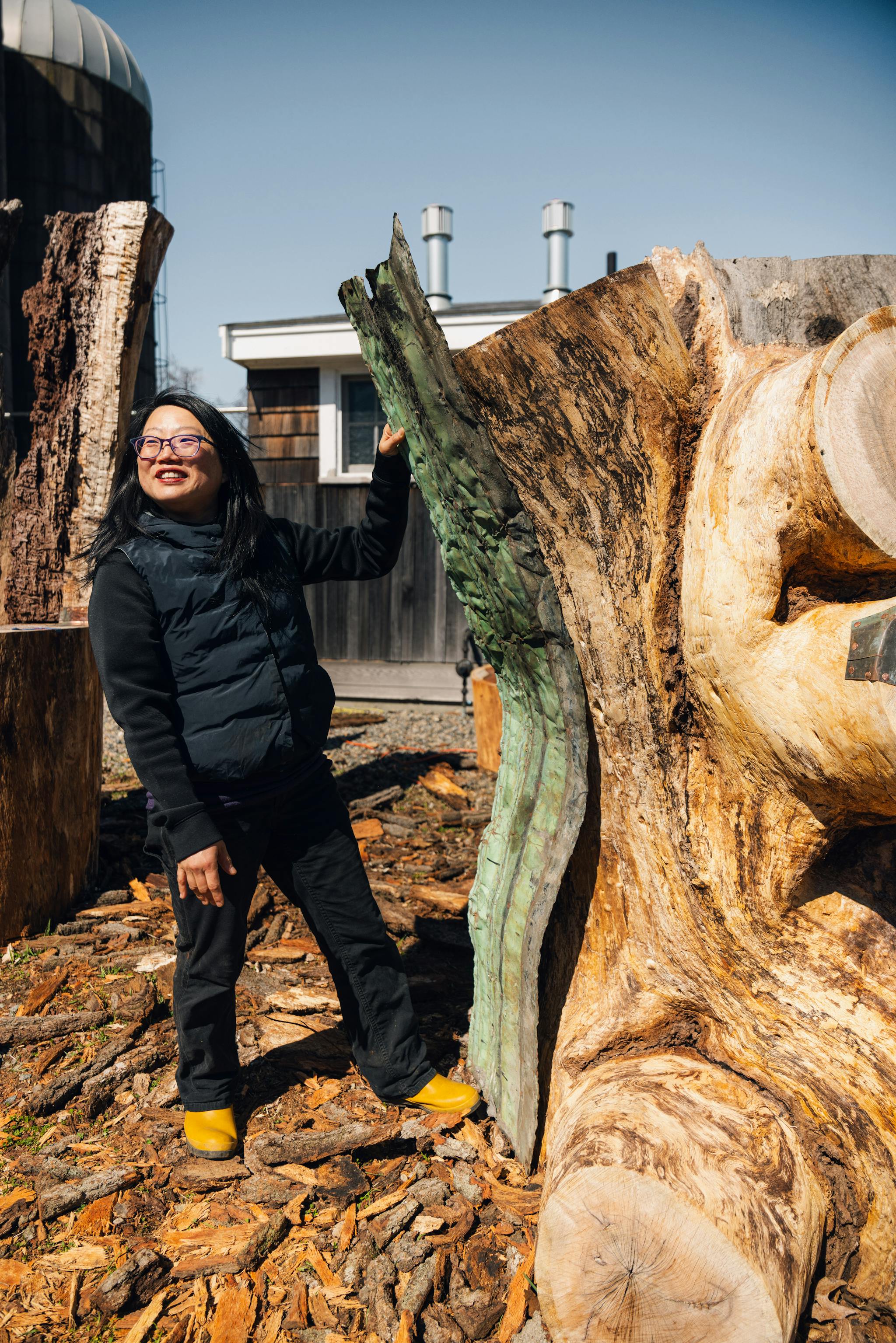Korean American artist Jean Shin stands beside a large leaning tree stump—one of the pieces she's working on on site at Appleton Farms.