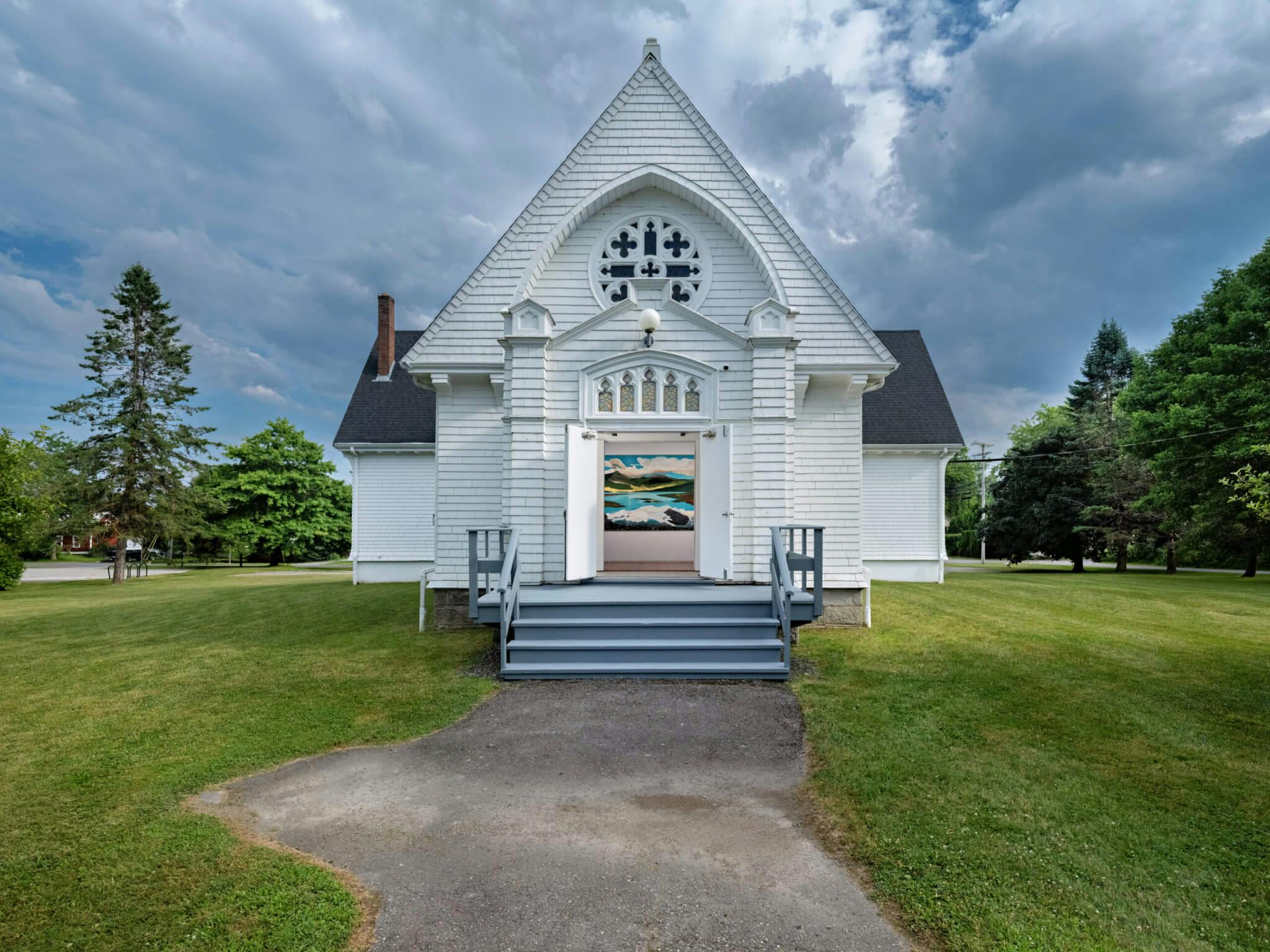 An exterior view of a small white church holding an art exhibition.