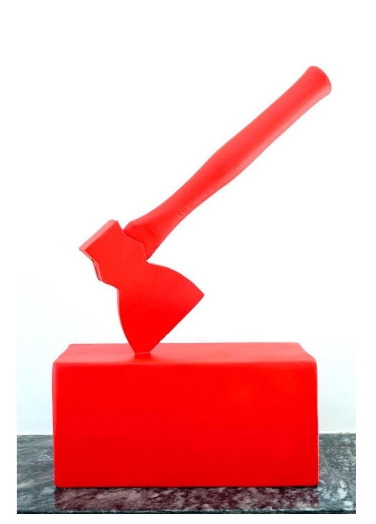 Image of a bright red sculpture that resembles an ax on a block.
