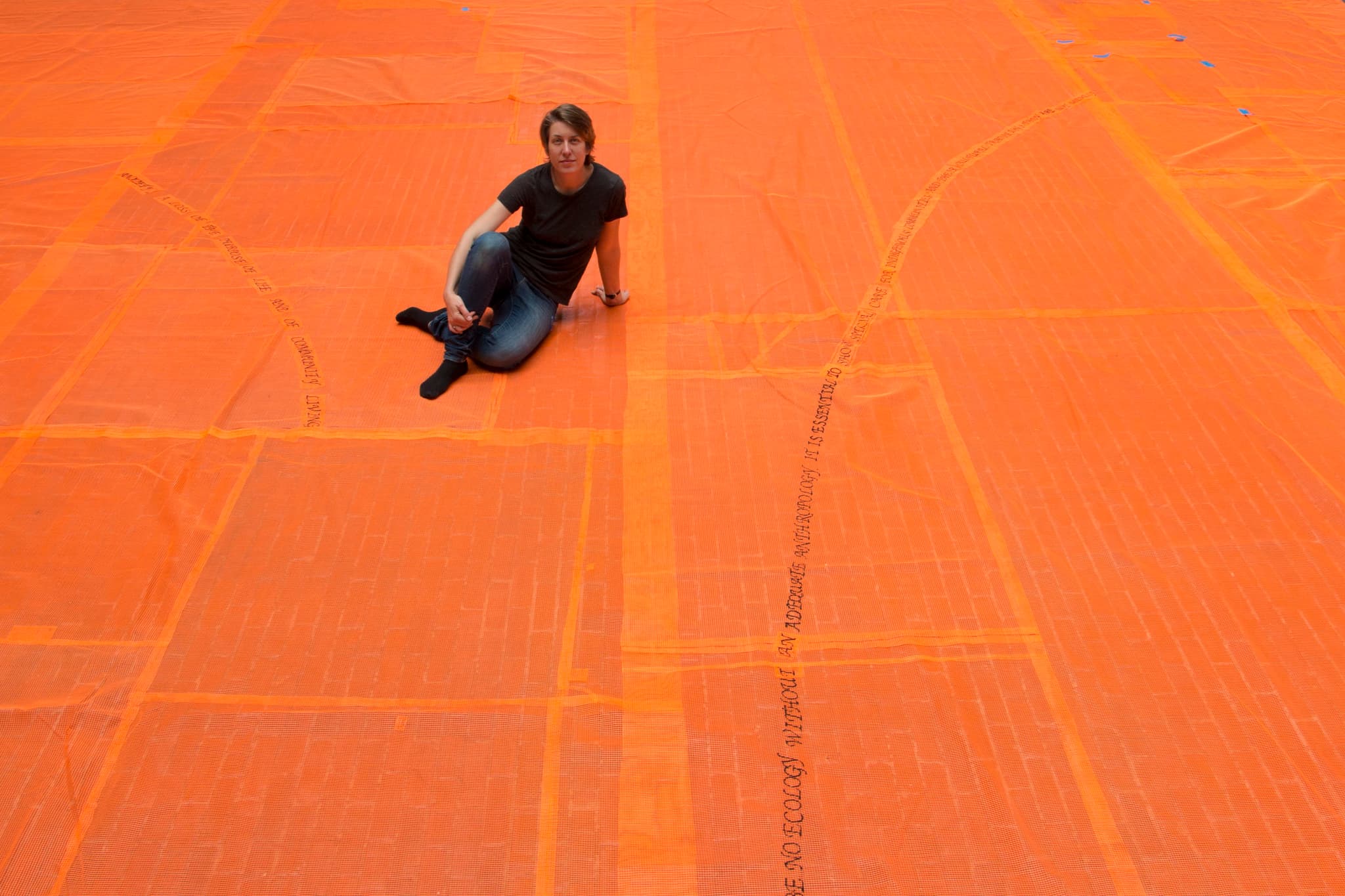 Stephanie Cardon sits on the orange, embroidered netting featured in her installation.