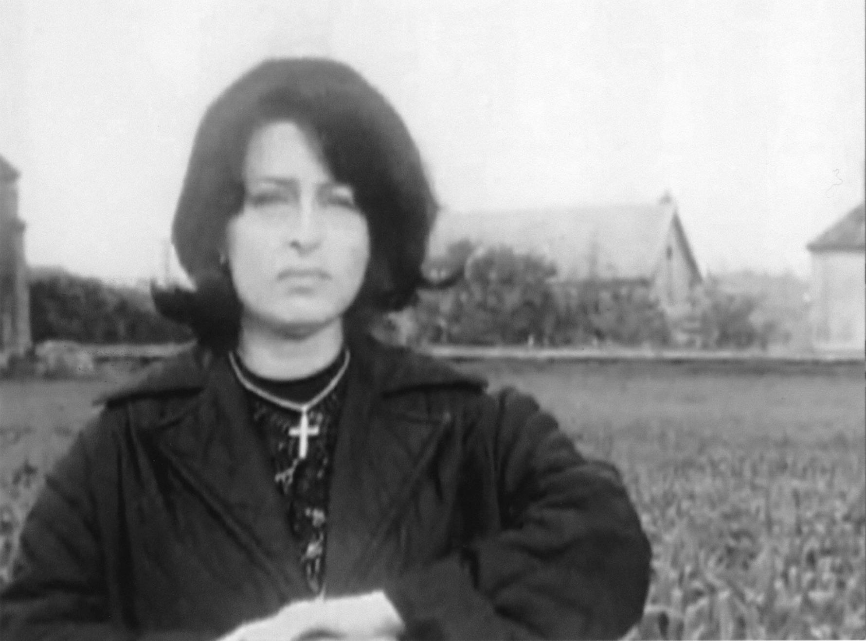 The black and white image of a woman standing in front of a rural scene.