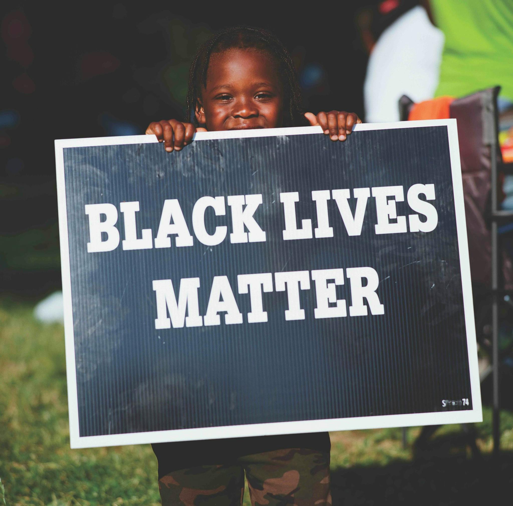 A child holds up a Black Lives Matter sign, while standing on green grass.