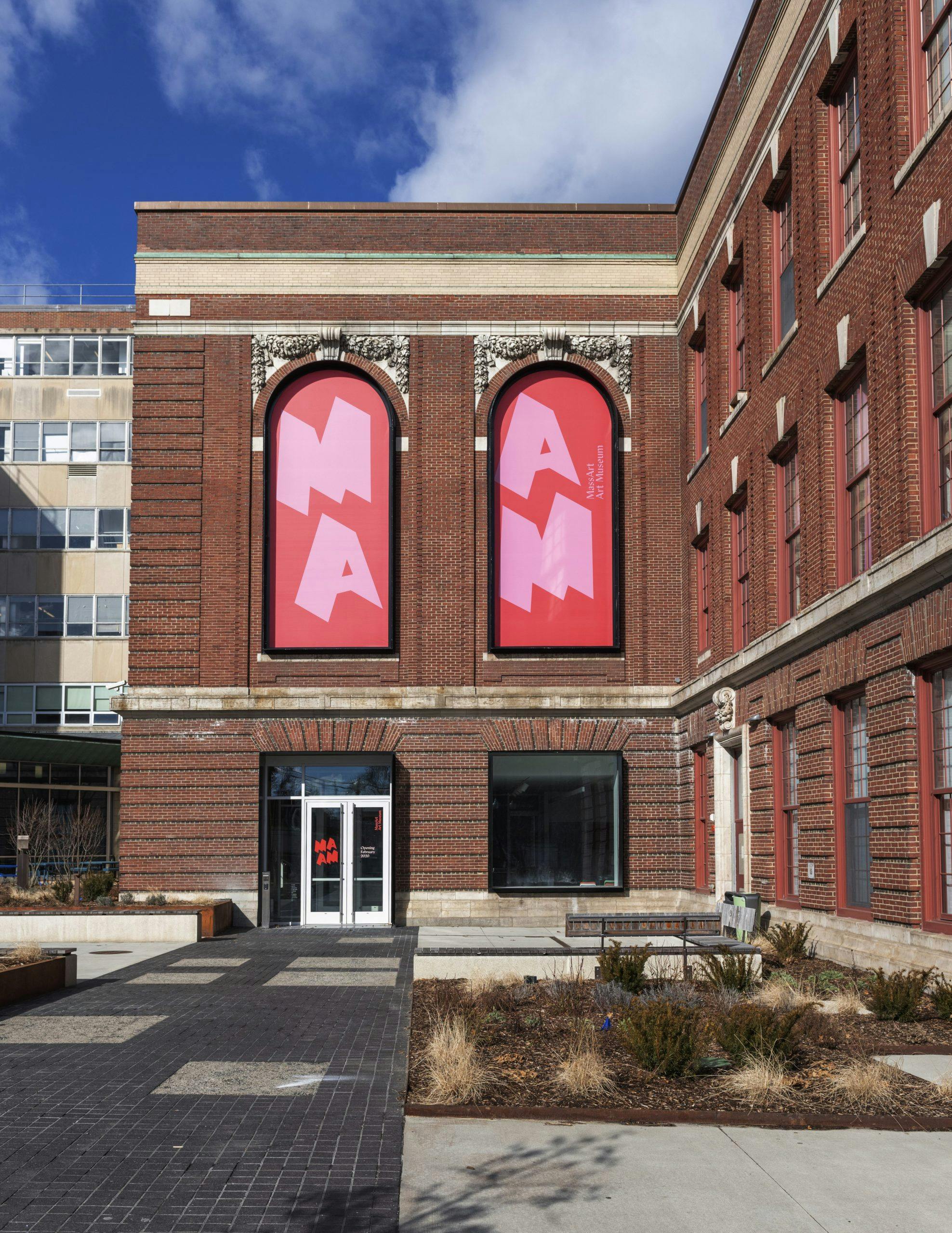 The red brick building of MAAM, displaying red and pink signs in the arched windows.