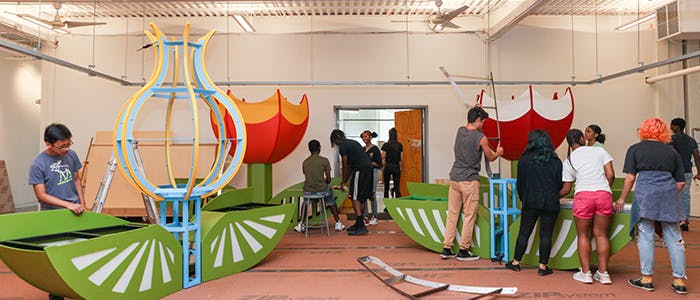 Figures are building boldly colored flower benches in a workshop space.
