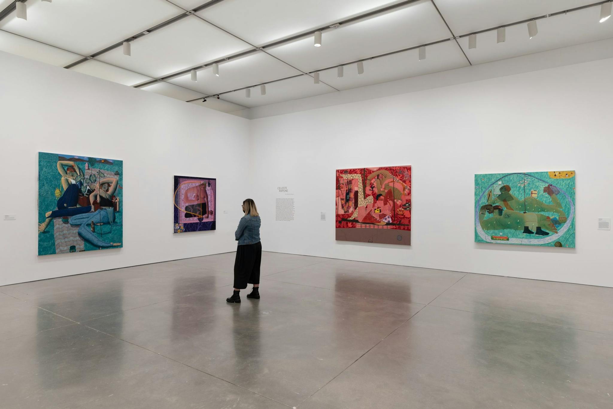 A woman stands in the center of the gallery space, taking in figurative paintings.
