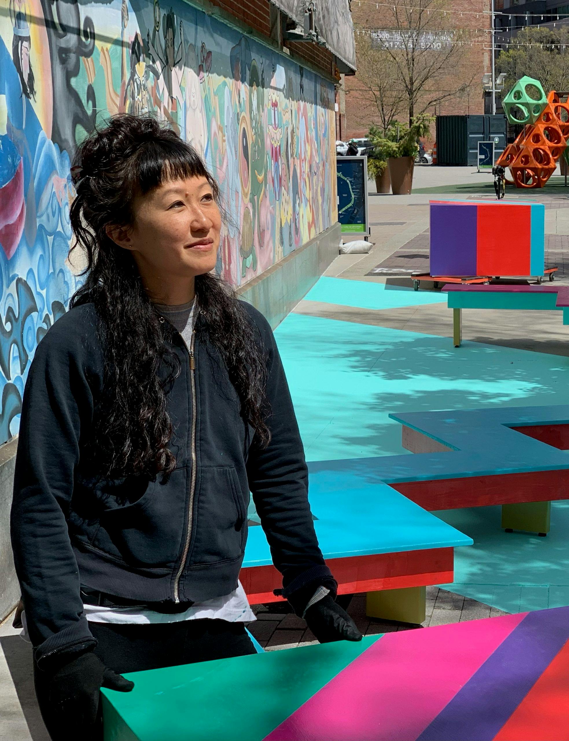 Cheryl Wing-Zi Wong stands with a colorful public work of art behind her.