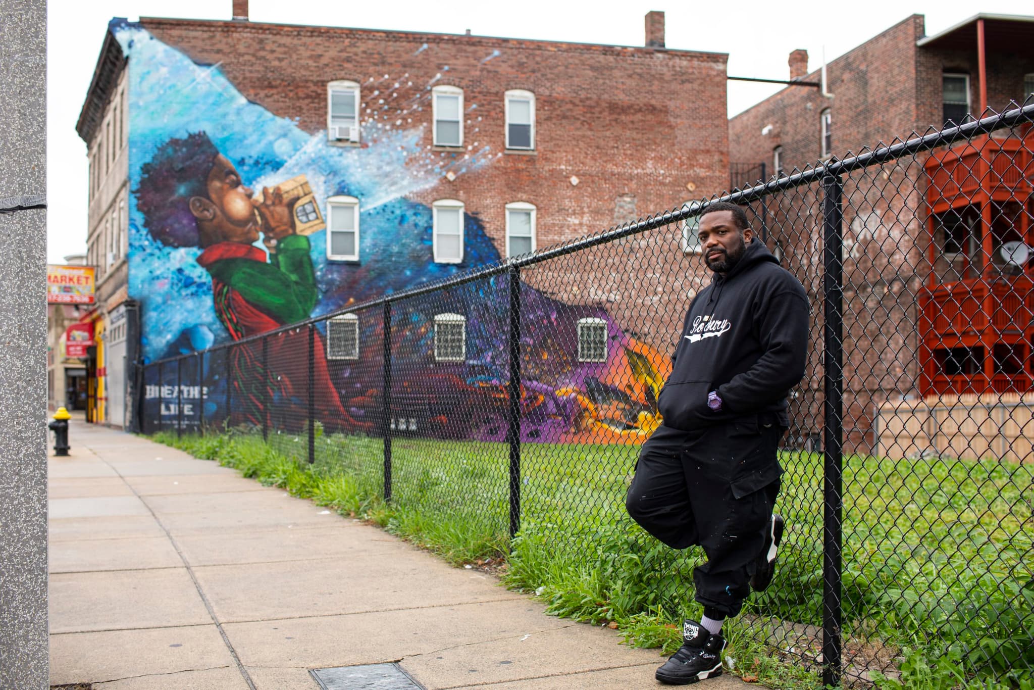 Artist Rob “ProBlak” Gibbs leans against a fence near his public art piece, a mural called Breathe Life.