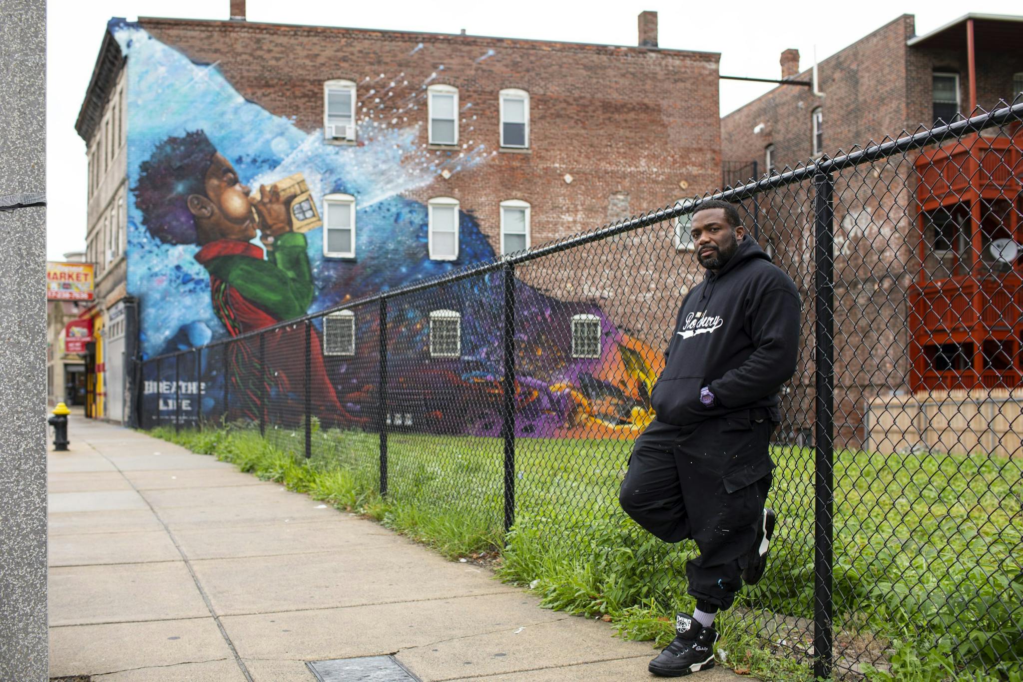 Artist Rob “ProBlak” Gibbs leans against a fence near his public art piece, a mural called Breathe Life.