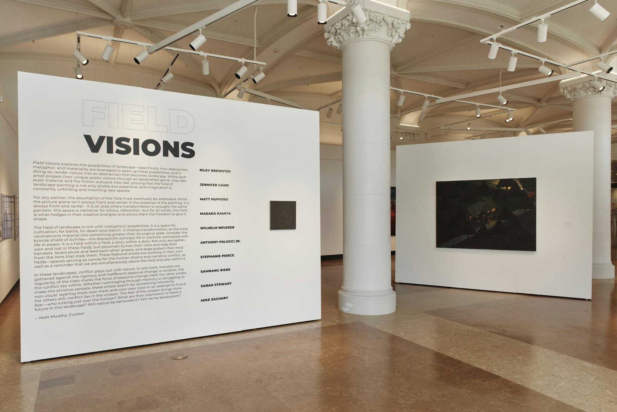 On a large white board positioned in front of a Greek column, text explains the "Field Visions" exhibit.