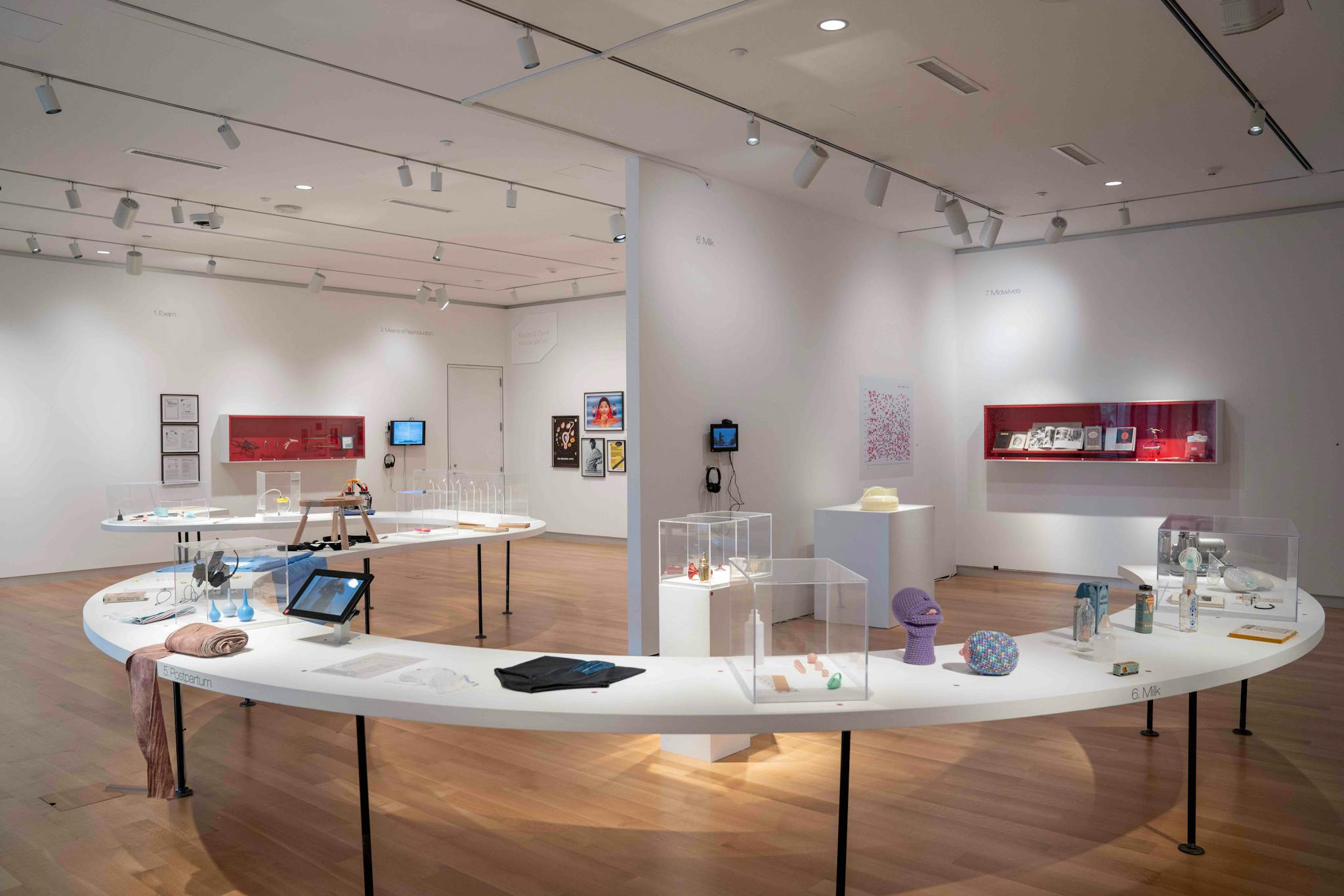 Objects relating to motherhood on display on a white curving table and positioned against the walls of the gallery.