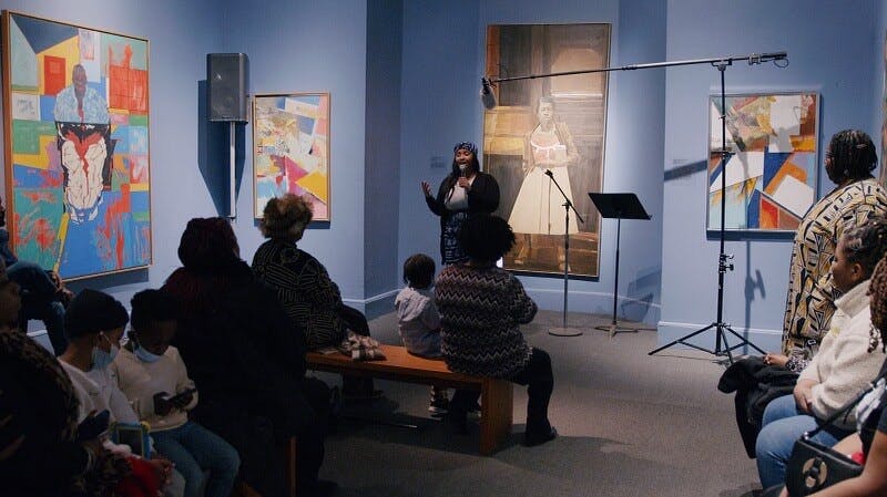 Singer Ashley Villard performs in front of an audience in a room that displays artwork on the walls.