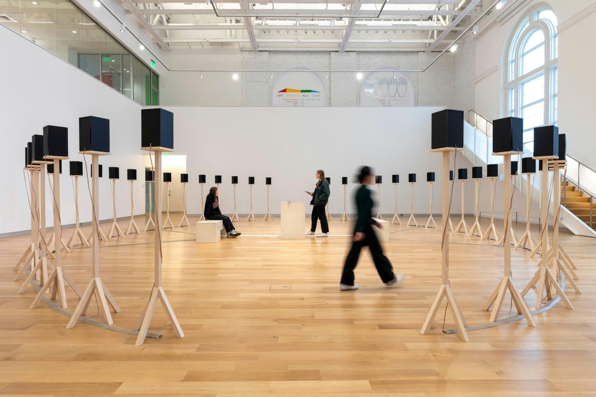 Forty speakers rest on stands, while three figures are positioned throughout the installation.