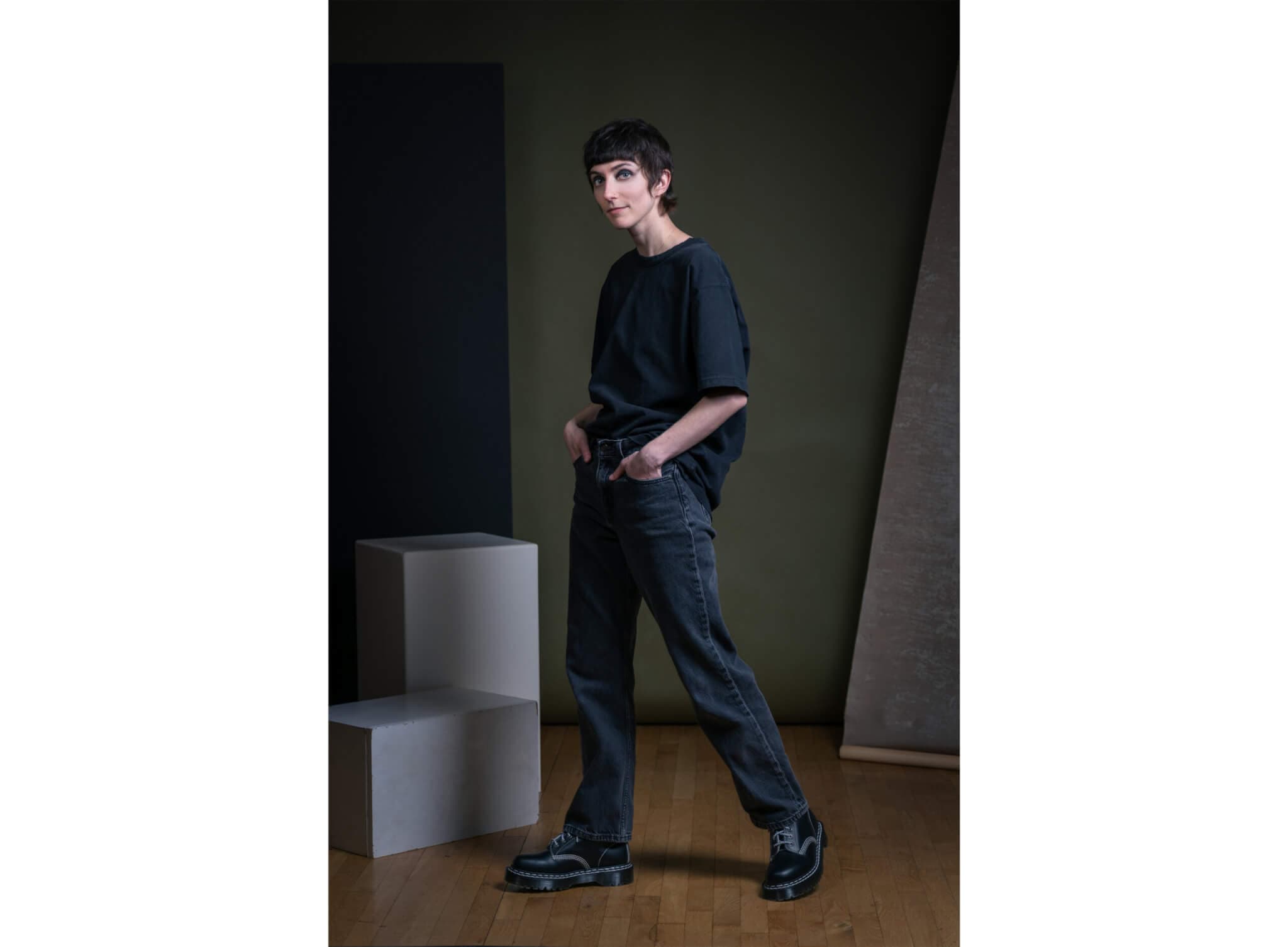 Georden West wears dark attire, standing beside two cubes, hands in pockets.