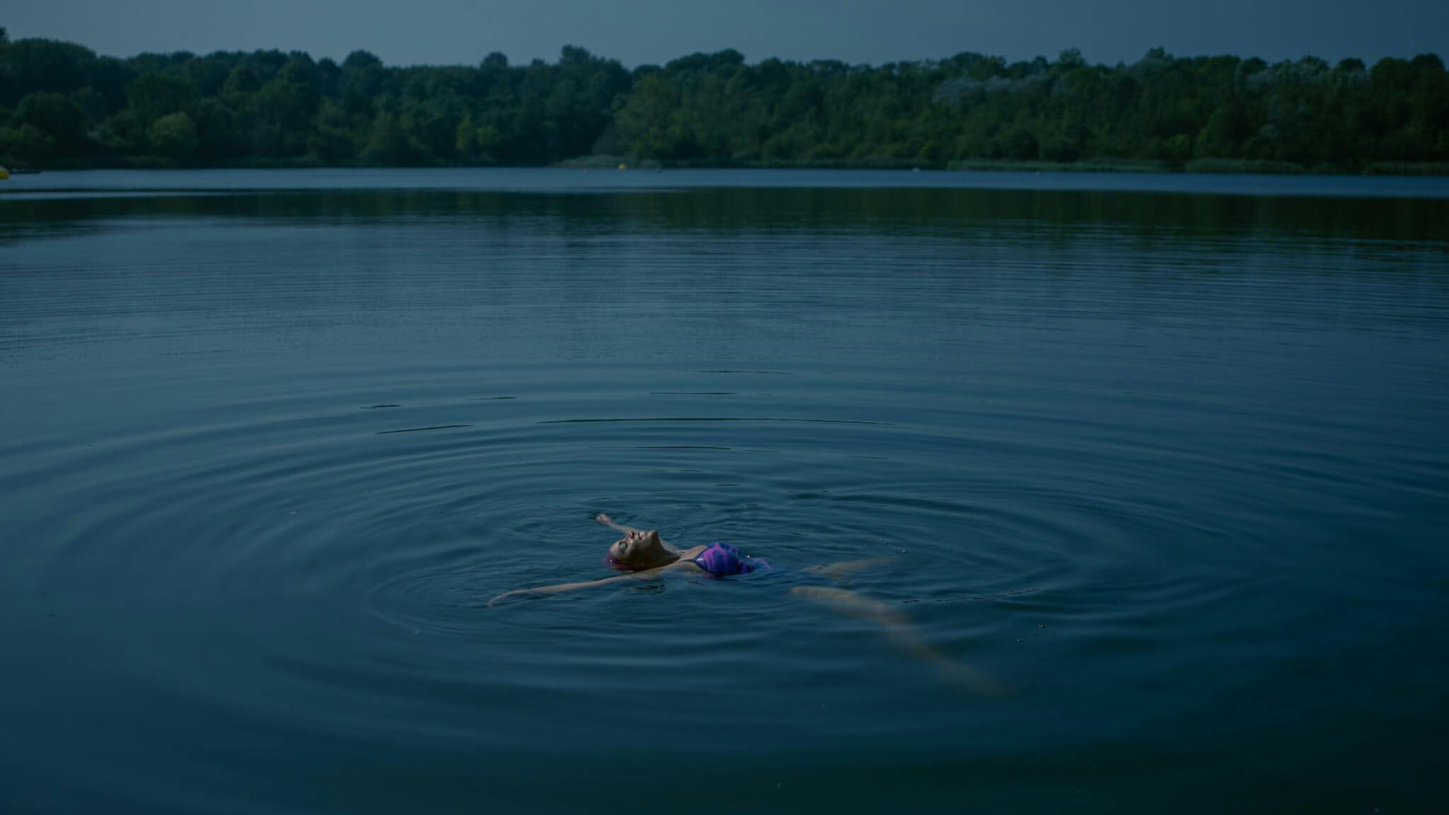 A Black woman floats alone in a deep blue body of water, in a film.