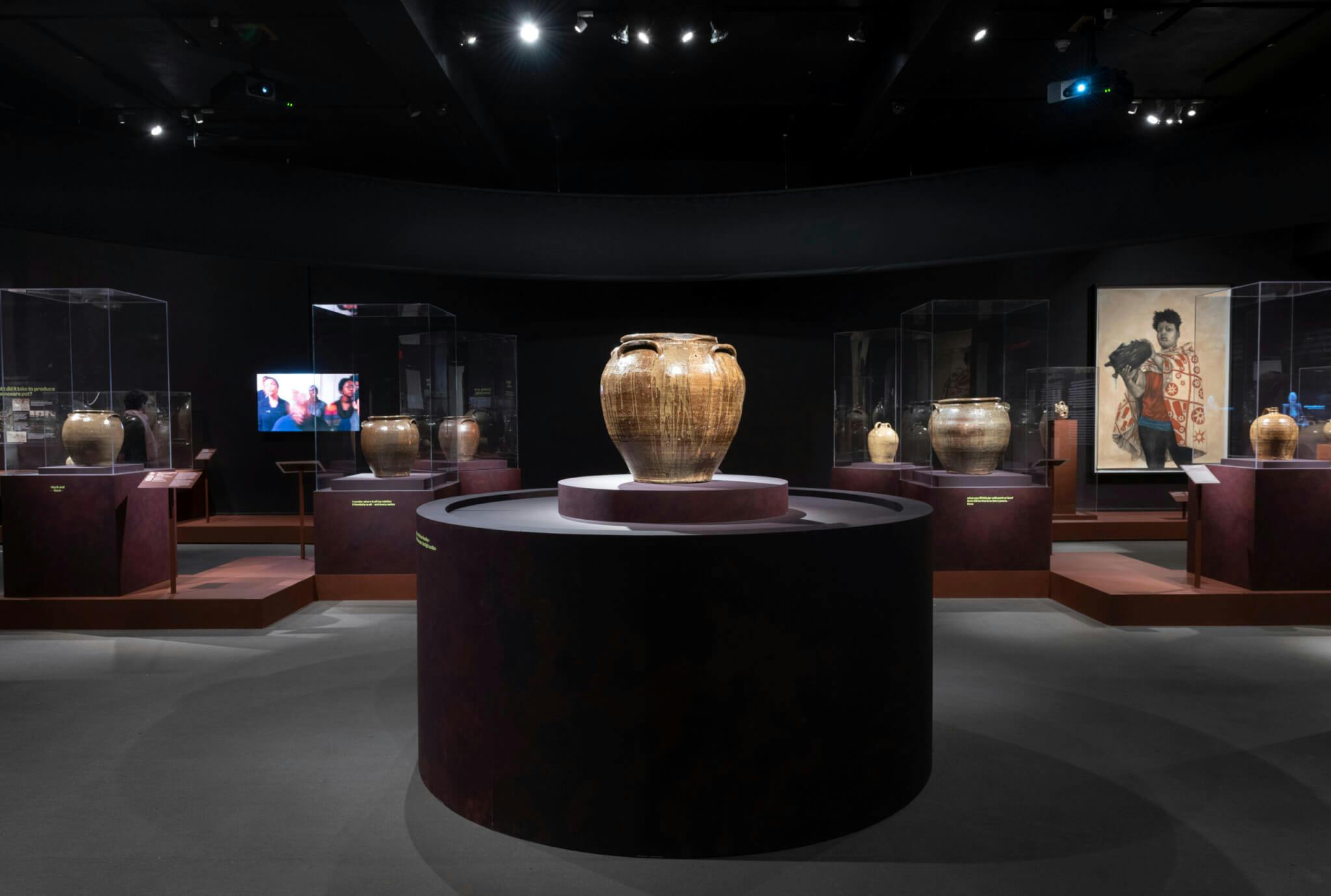 In the center of the image, a ceramic vessel stands on a black pedestal at the Museum of Fine Arts.