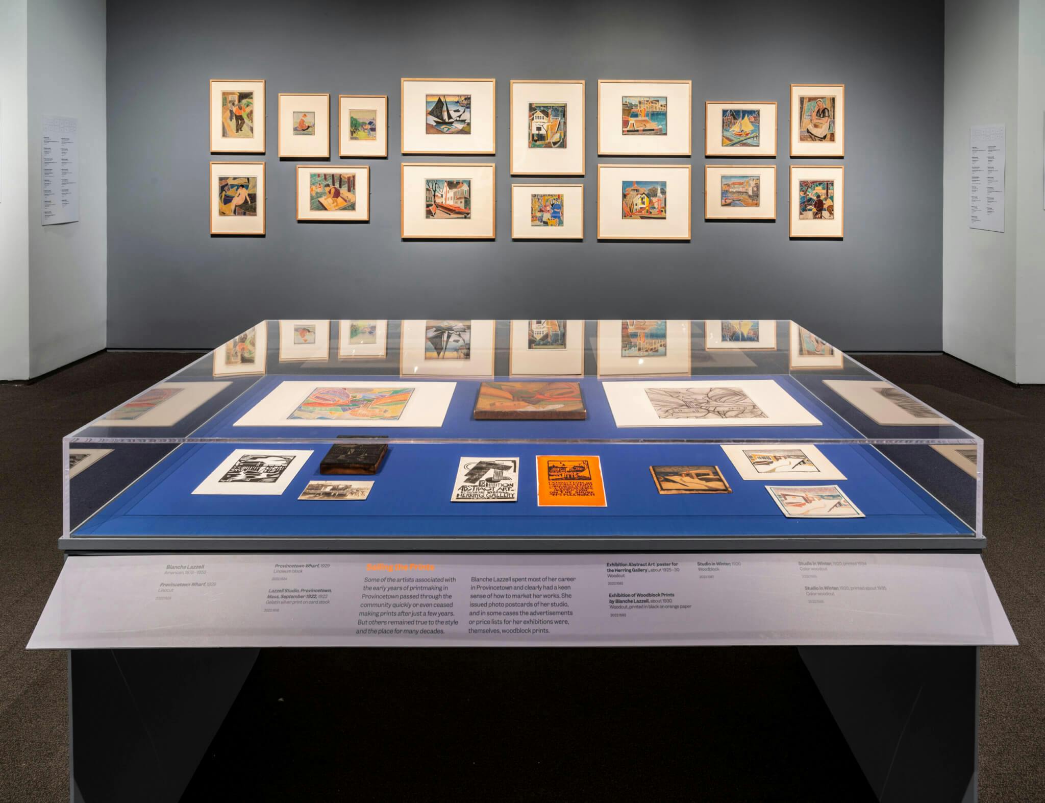 Prints on display within a glass case and lining a gray wall at the Museum of Fine Arts.