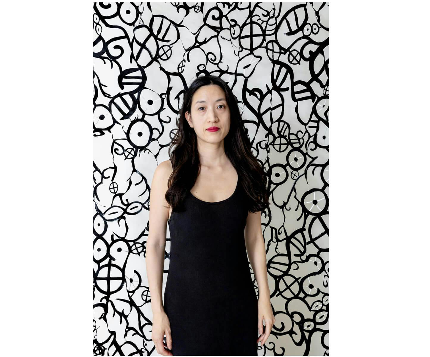 Jocelyn Shu wears black, standing in front of a patterned black and white background.