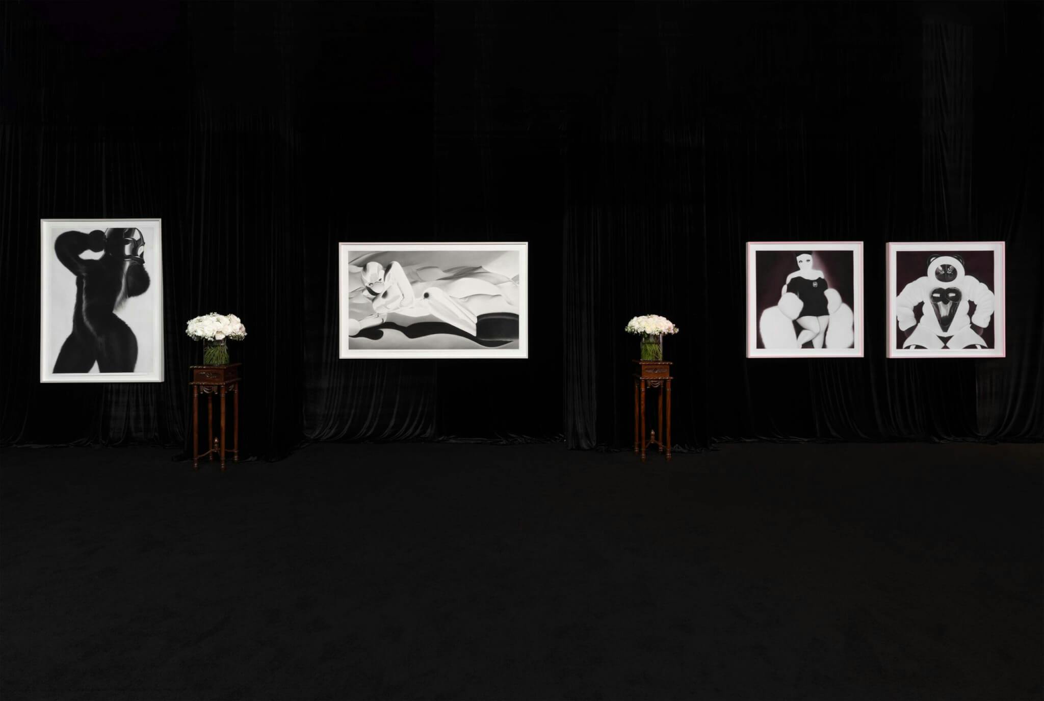 Black and white images by Katrina Pisetti and Josh Allen, set against a black background, with stands bearing white flowers in between.