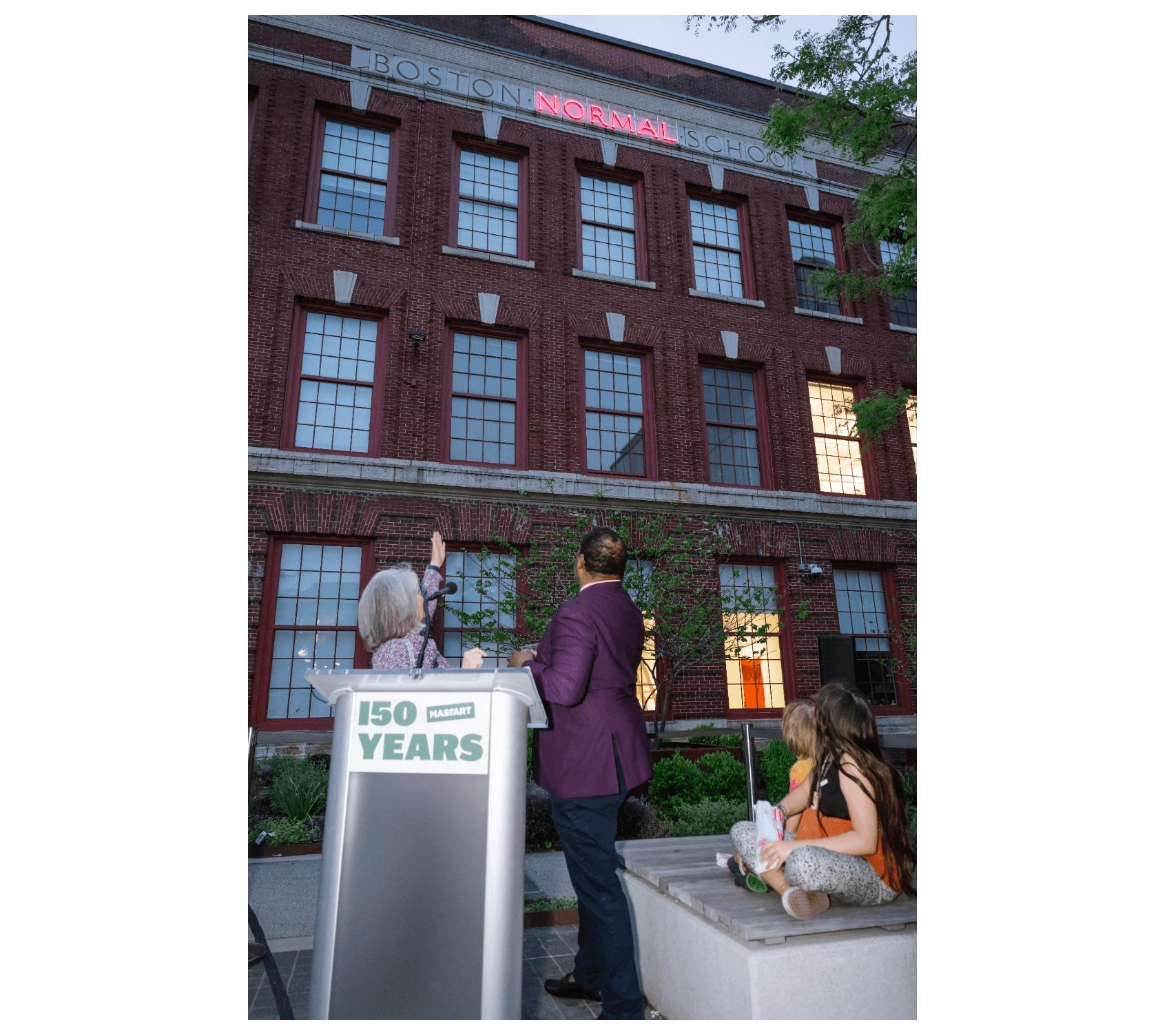 MassArt President Mary K. Grant and artist Steve Locke stand in front of a building with the sign "Boston Normal School."