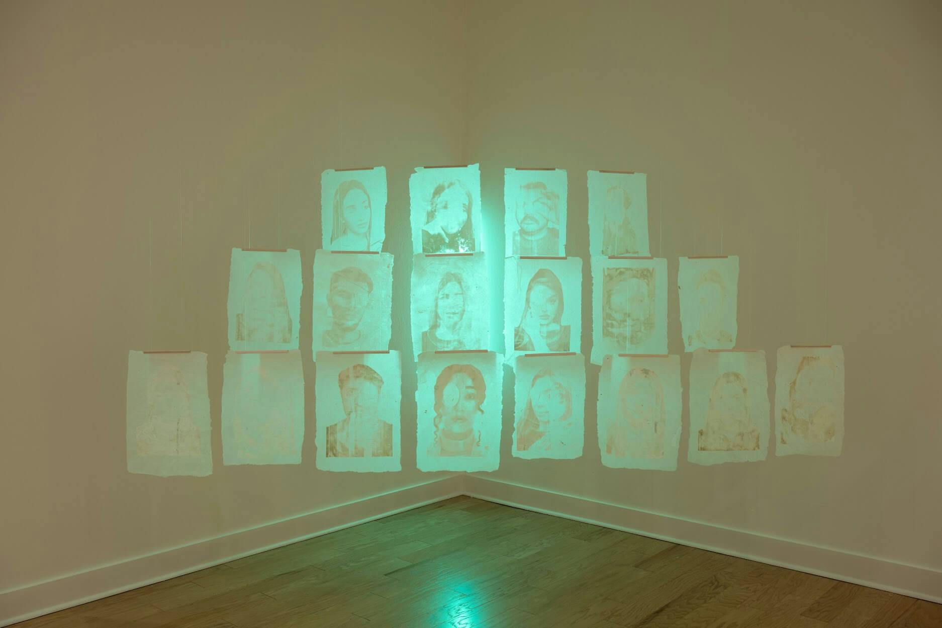 A squat pyramid of prints faintly etched with faces, lit up by a green light coming from beneath.