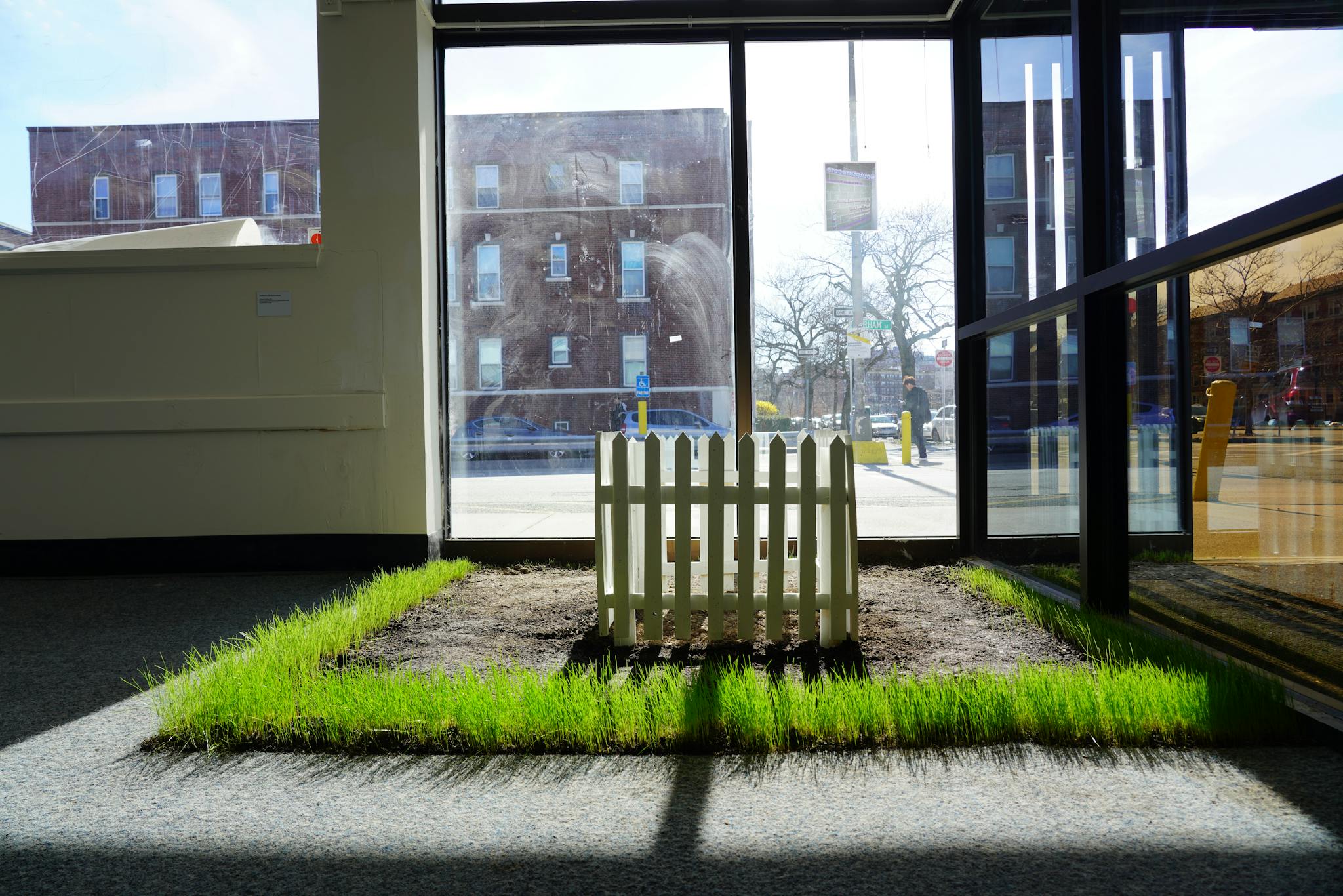 A white picket fence emerges in a patch of green grass in the indoor exhibition space.